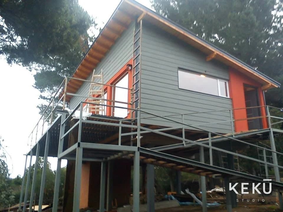 Vivienda elevada con revestimiento gris y aberturas rojas